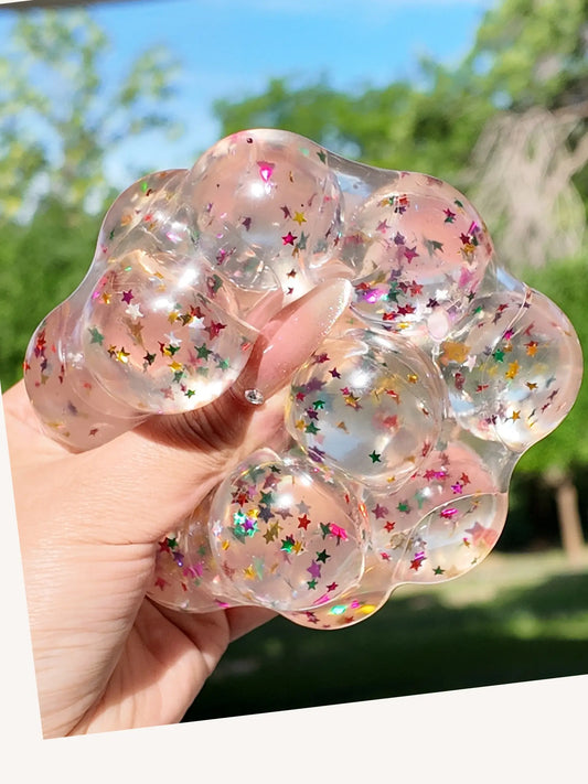 Lovesquishy clear silicone squishy with colorful star confetti, held by hand outdoors