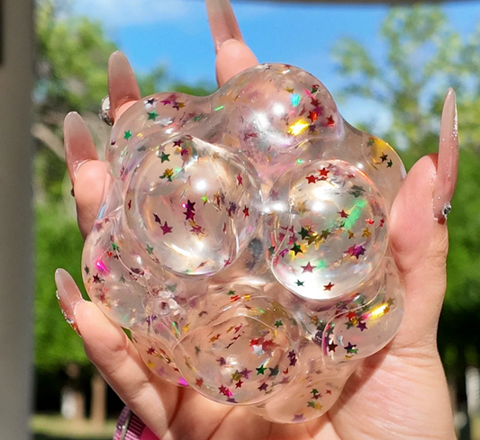 Lovesquishy clear silicone squishy with colorful star confetti, held by hand outdoors