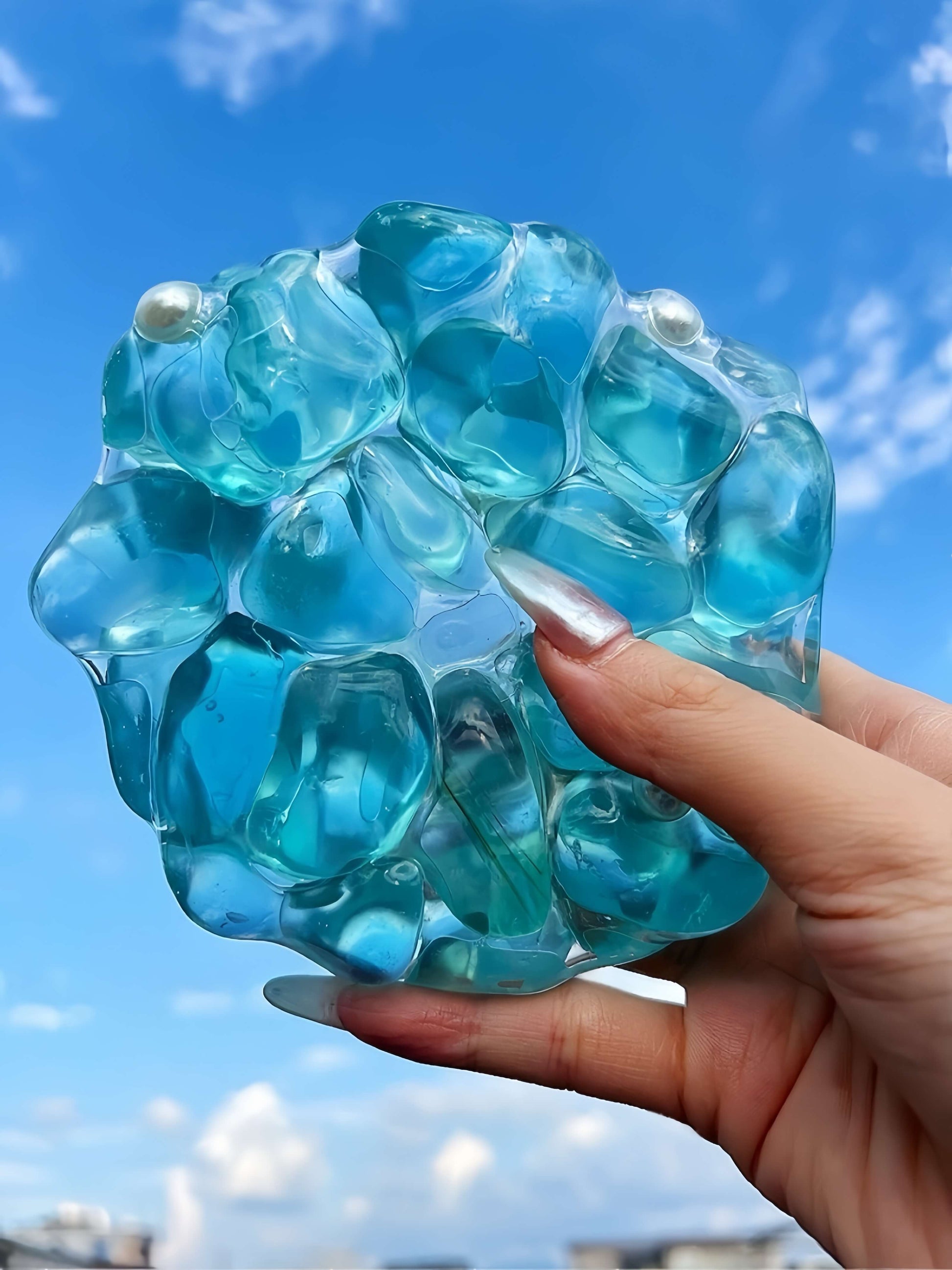 Handmade blue pearl jumbo squishy ball stress relief toy being squeezed outdoors