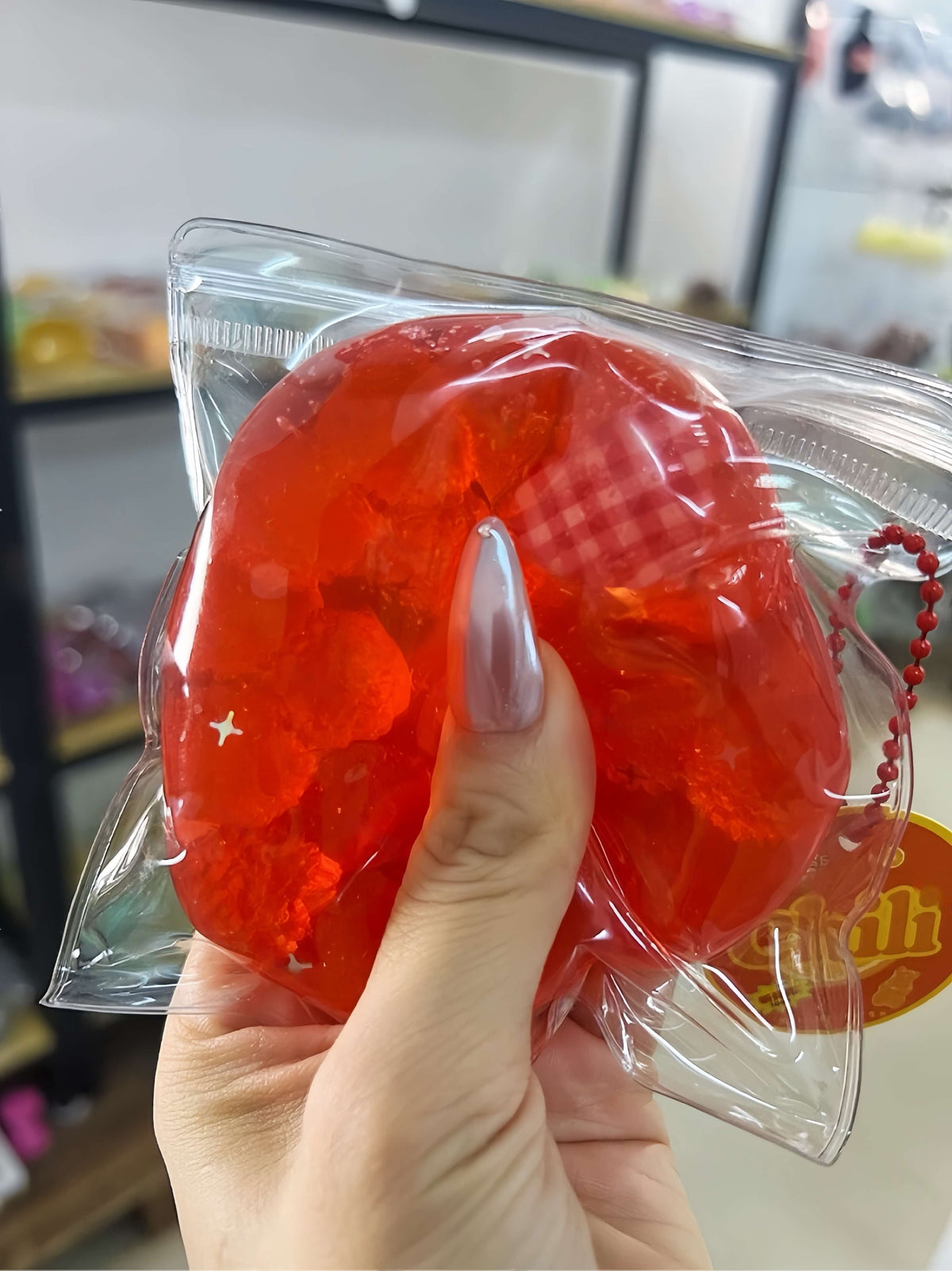 Hand holding red squishy fruit jam hard candy ball in clear packaging, stress-relief toy by Lovesquishy