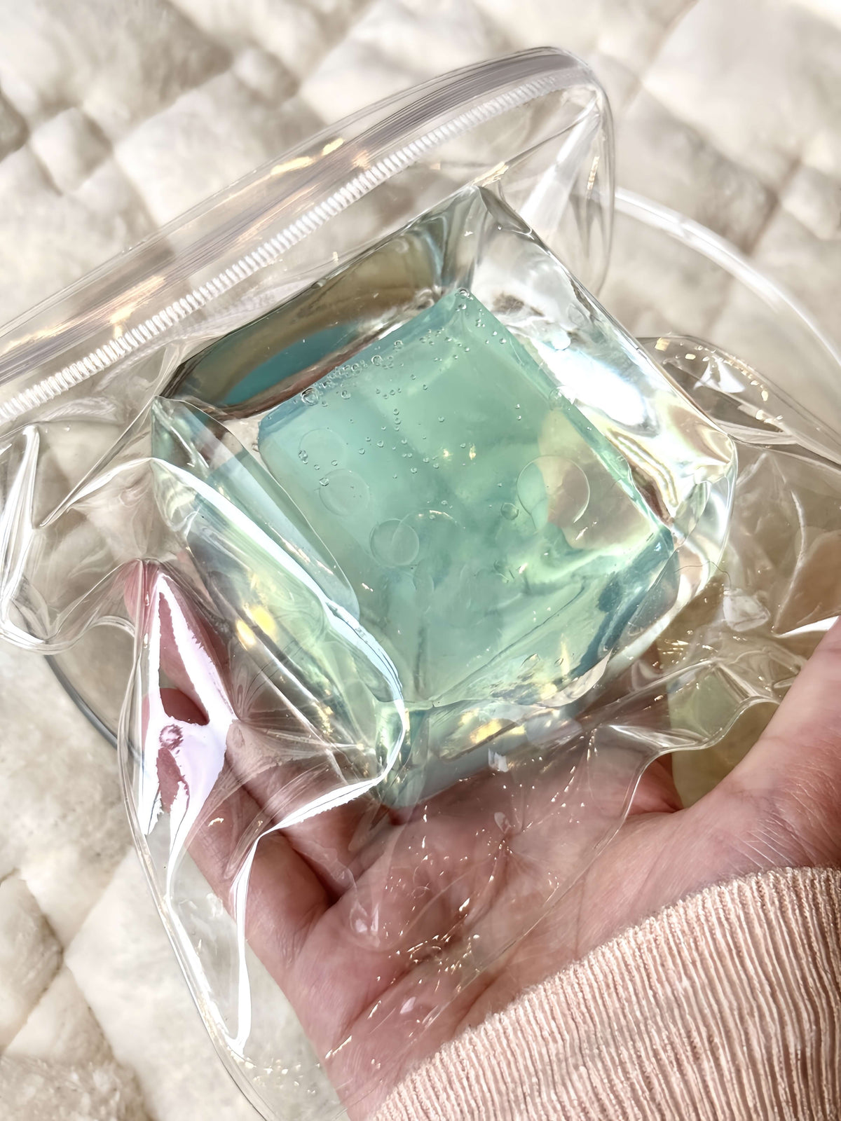 Hand holding clear bag with sunny green grape flowing sand ice block, ultra-soft squishy toy with bubbles